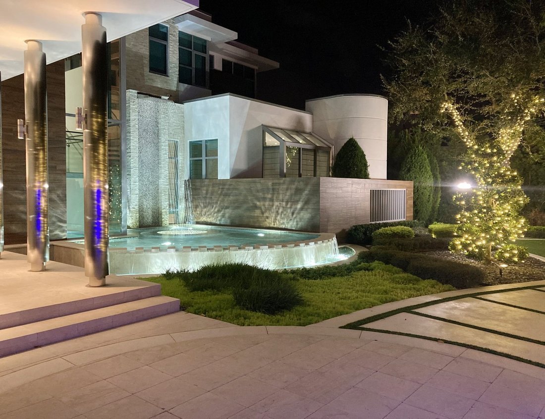 Modern white estate with uplit trees and a fountain at night, St. Petersburg holiday lighting